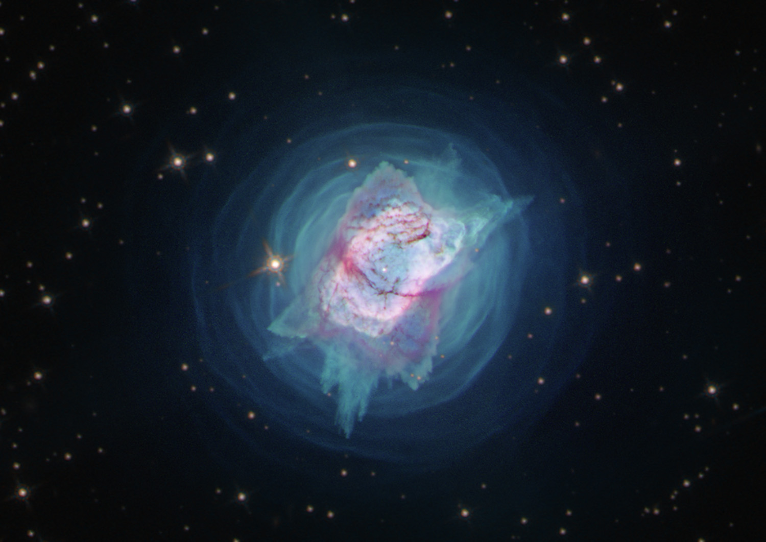 Concentric rings of teal light sit in front of a black backdrop dotted with stars. At the center of rings lies a multicolored, roughly rectangular feature with a mottled appearance.